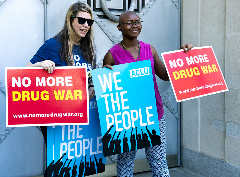 picture of two women holding up signs for the No More Drug War protest in front of the Justice Department, May 15, 2017