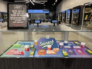 Display cases and touch screens in a One Plant cannabis dispensary. On the glass case is a sign that says, "Enter only if you are 19 years or older."The displays show different forms of cannabis, including flower, edibles, vape, and preroll.