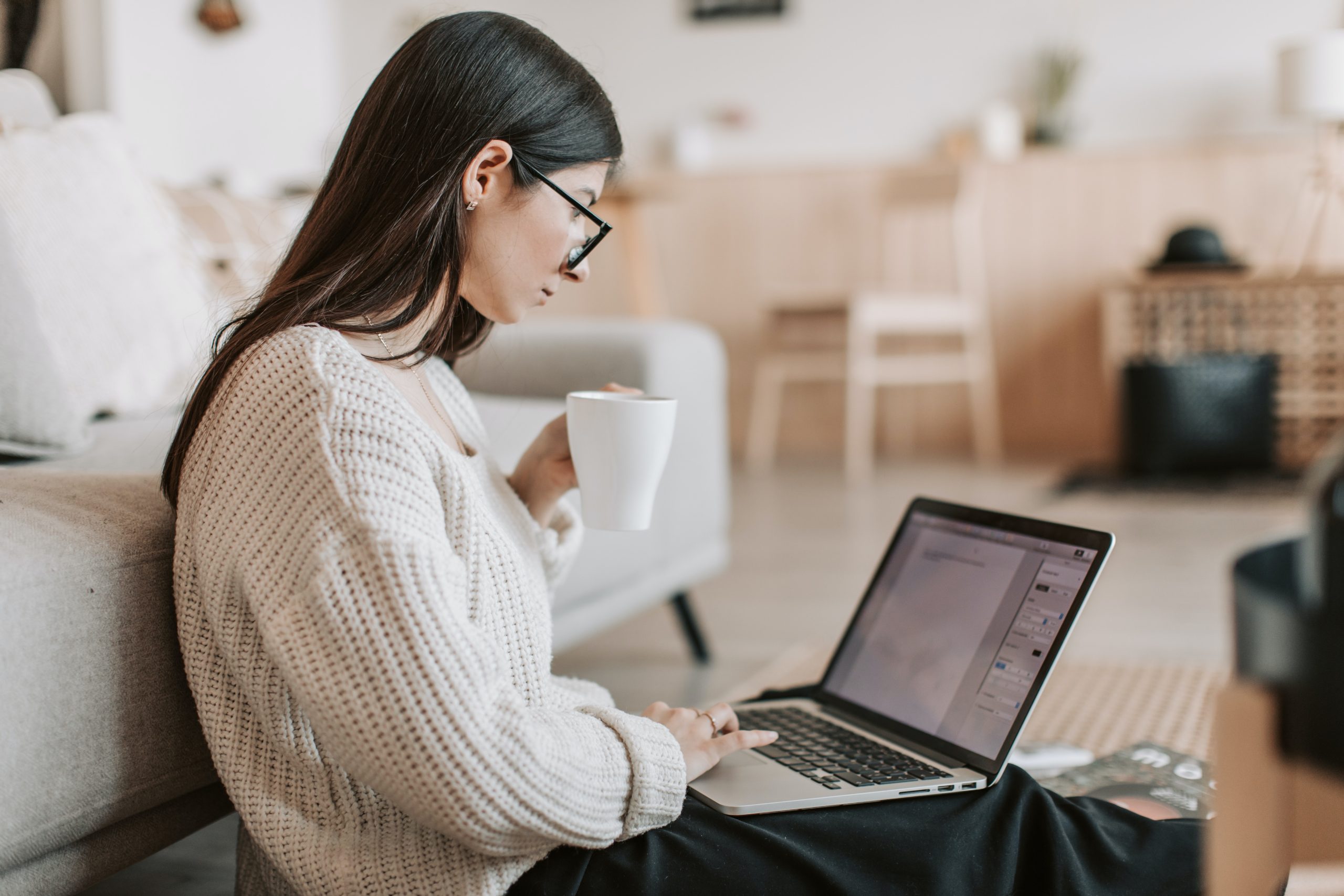 Woman holding a coffee is working on her computer.