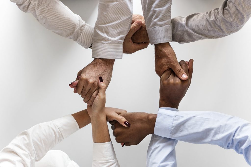 Image of four people holding hands criss crossed around a circle