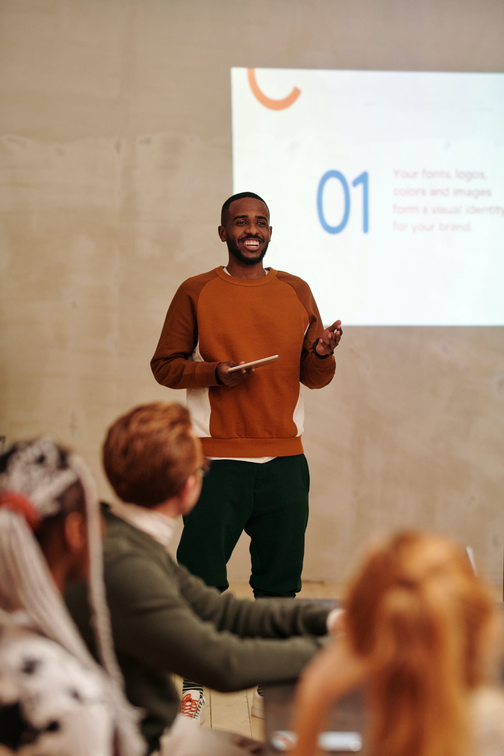 A man is standing in front of a slideshow. There are people in the audience watching his presentation.