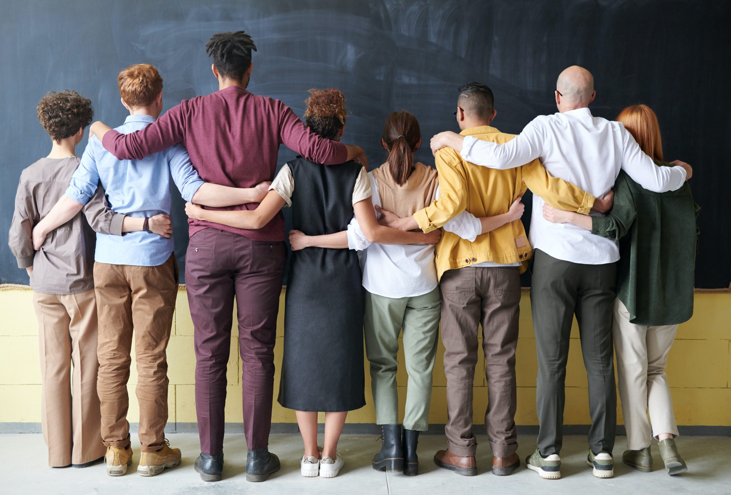 Diverse group of people standing inside facing away from the camera.