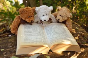 Three stuffed teddy bears sitting beside one another reading a story book.