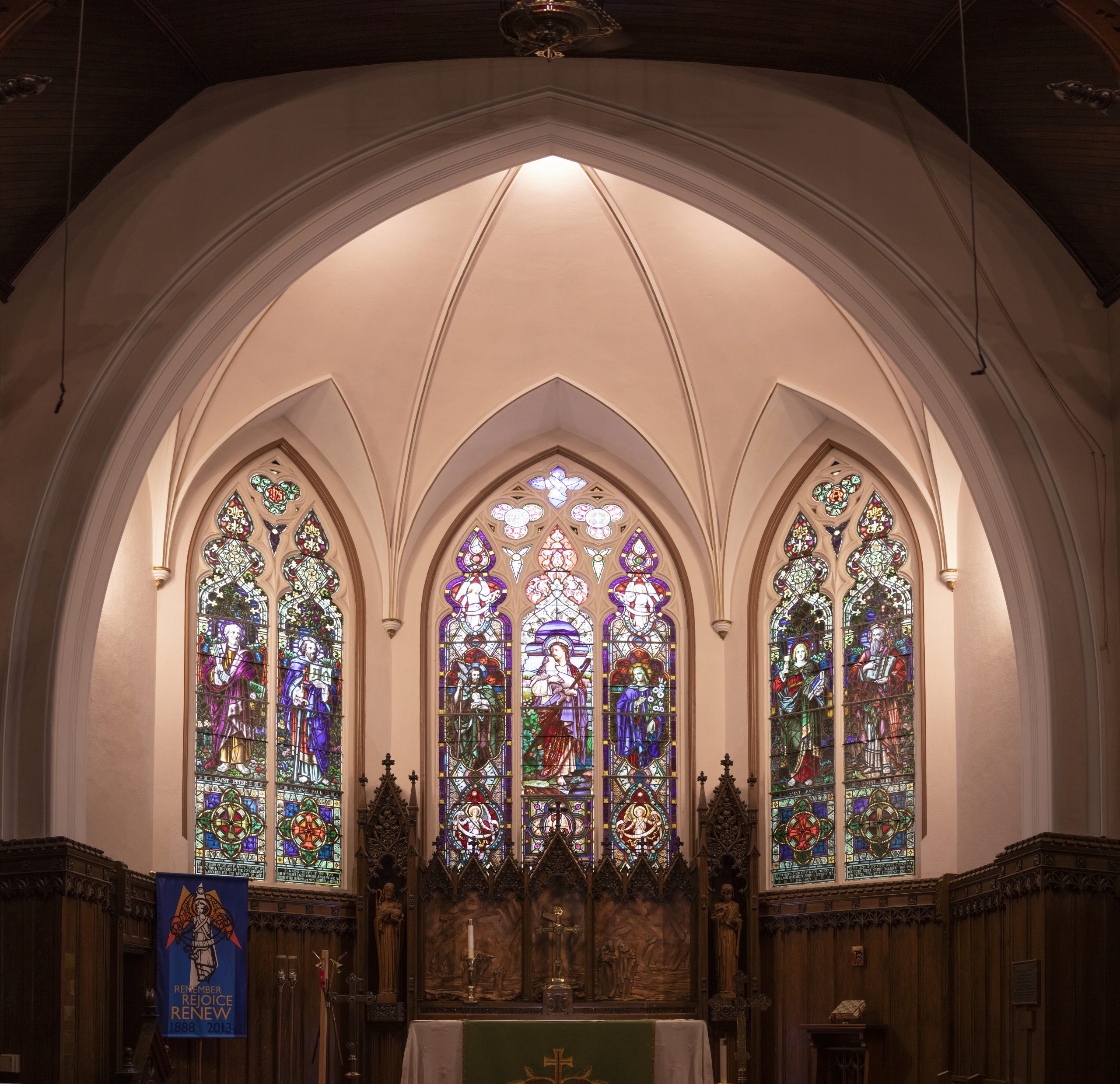 View of church chancel showing five stained glass windows.