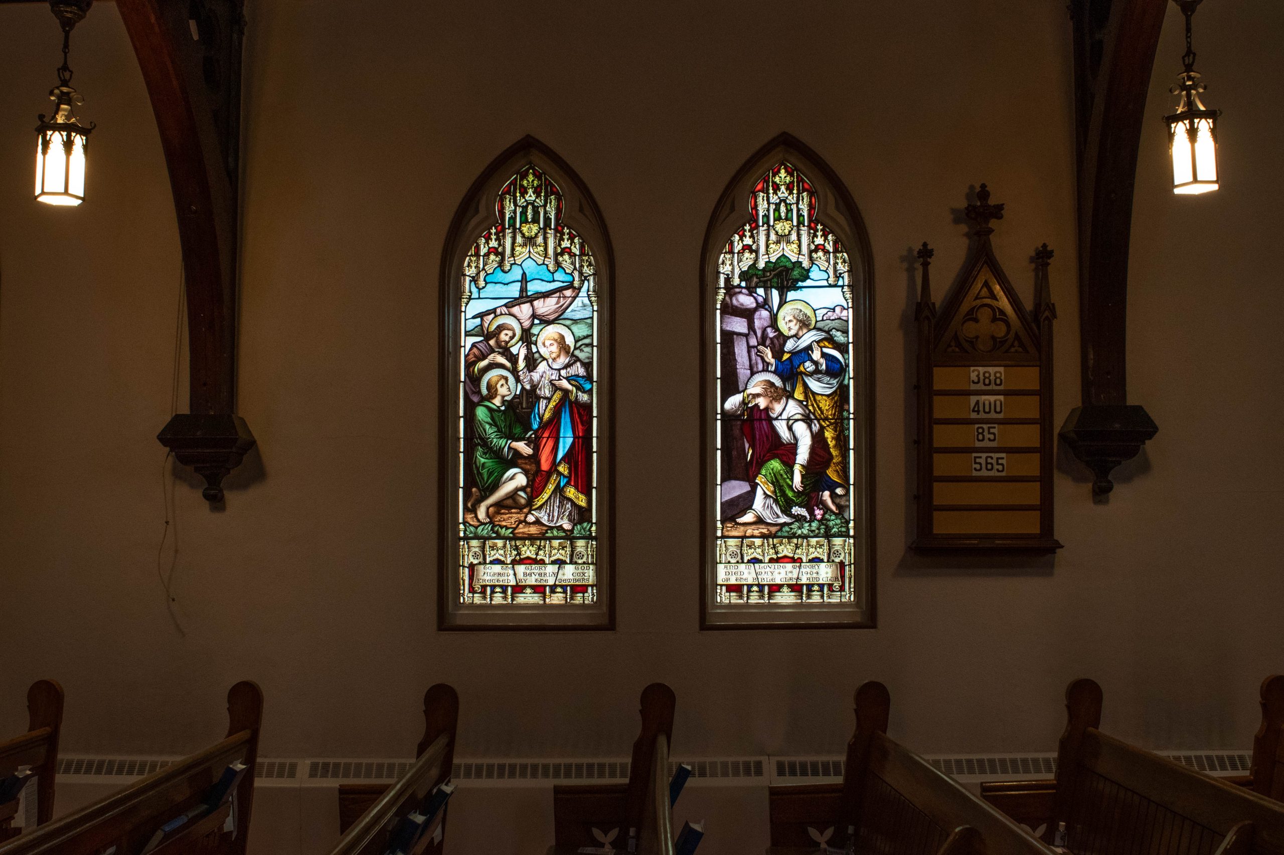 Two stained glass windows. One with three men in front of a boat. right window shows two men in front of a cave.