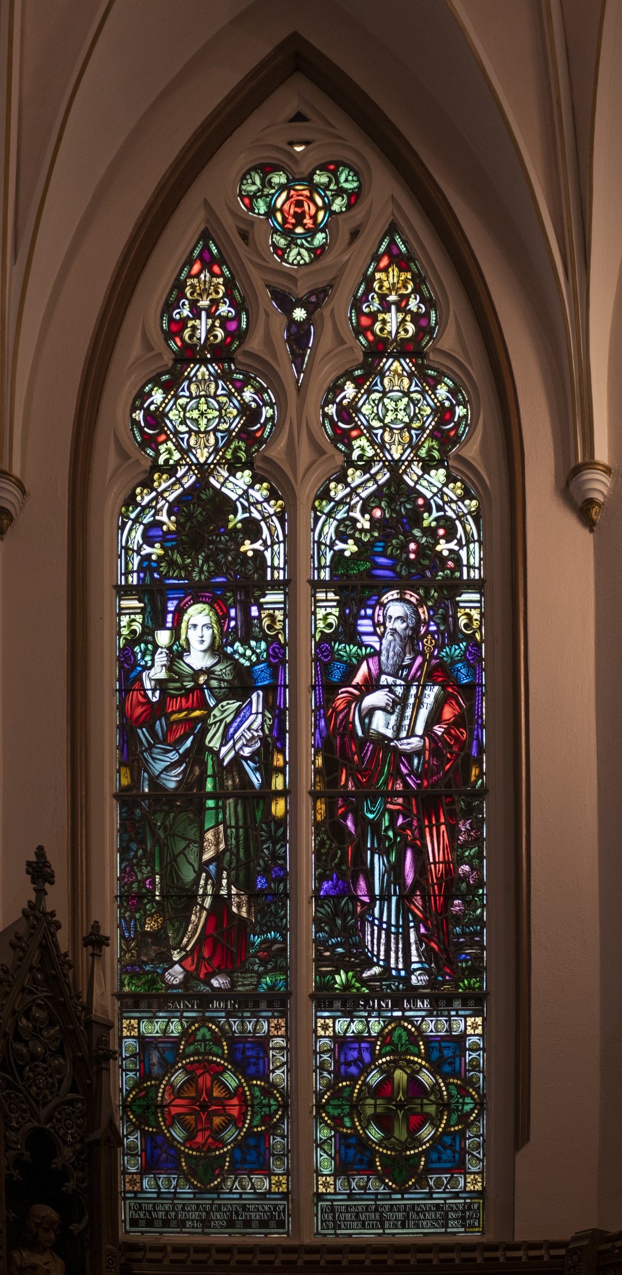 Stained glass window. Left side of window depicts a younger man holding a chalice and book. The right side depicts and older bearded man pointing to a words in a book.