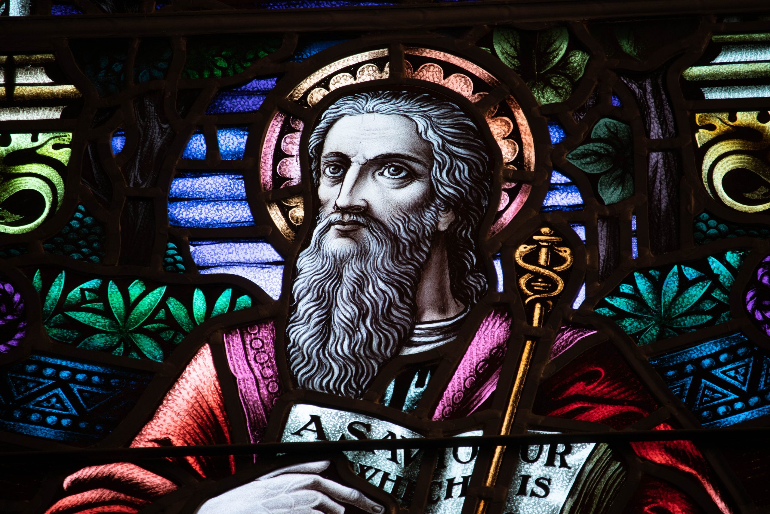 Detail of stained glass window with bearded man pointing to text in a book.