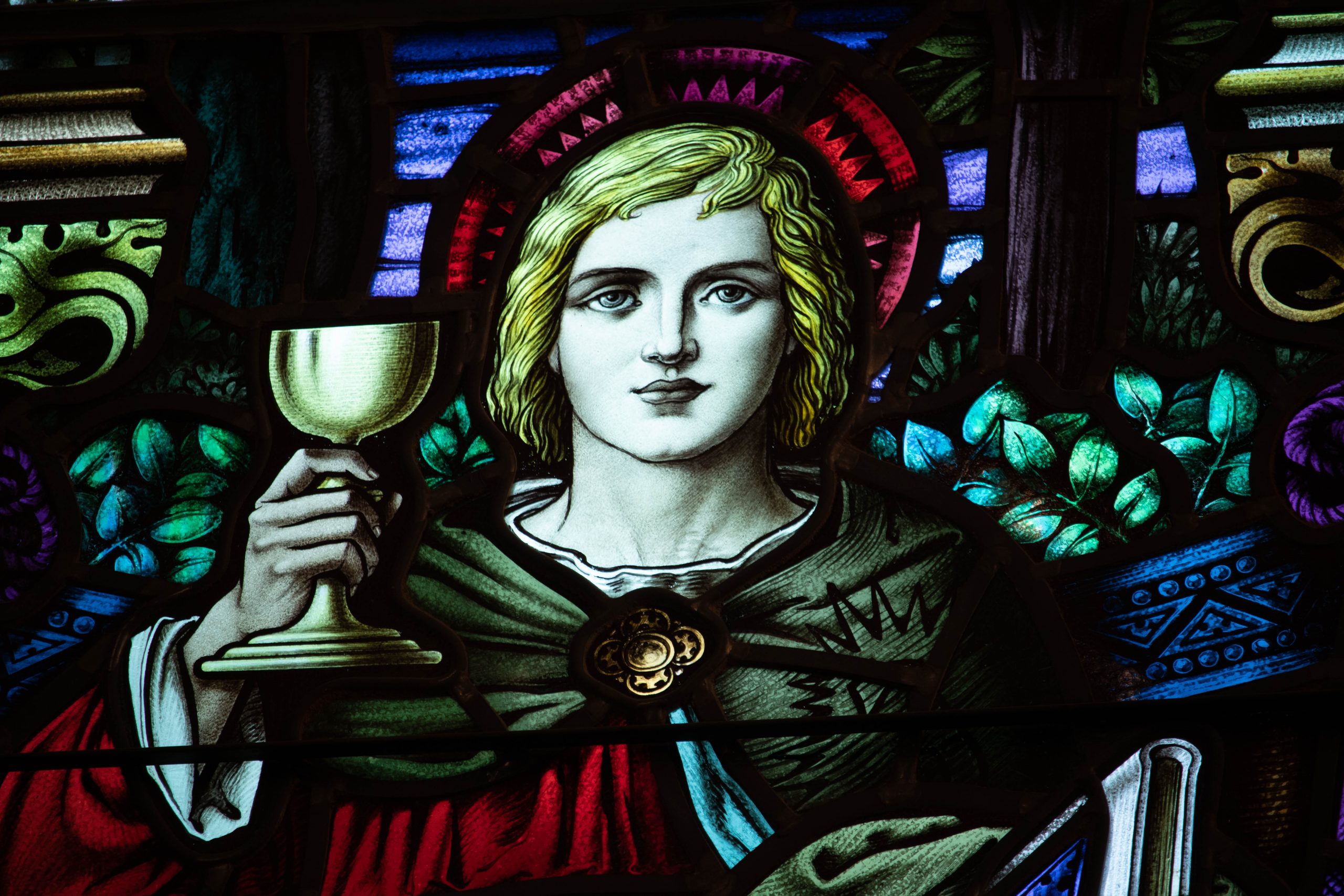 Detail of stained glass window with young man holding a chalice and a book.