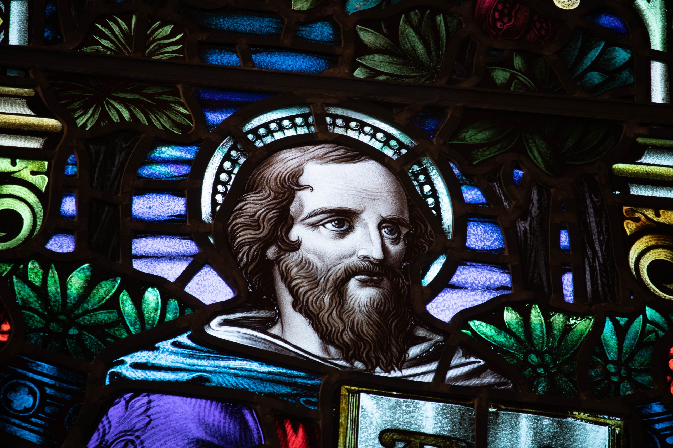 Detail of stained glass window showing head of a bearded male with a book.