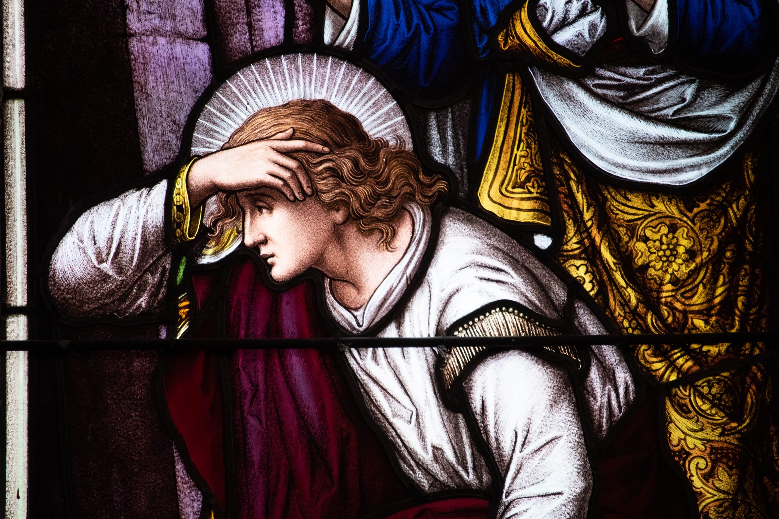 Detail of stained glass window showing torso and head of a young man looking into a cave.