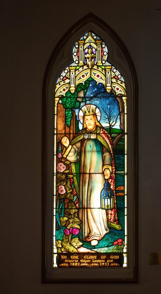 Window shows man knocking at a door while holding a lantern.