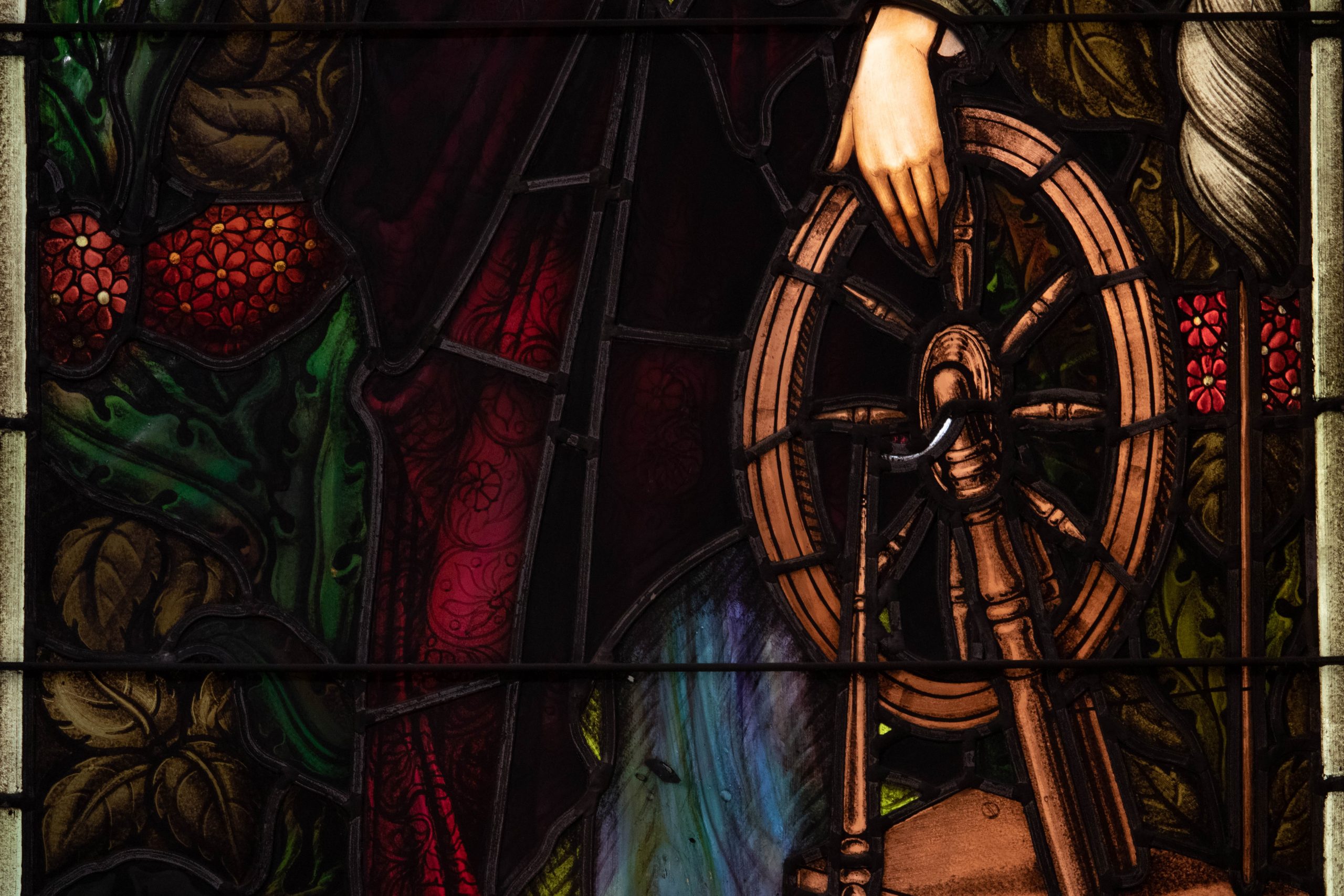 Detail of stained glass window showing a woman's hand holding a spinning wheel.