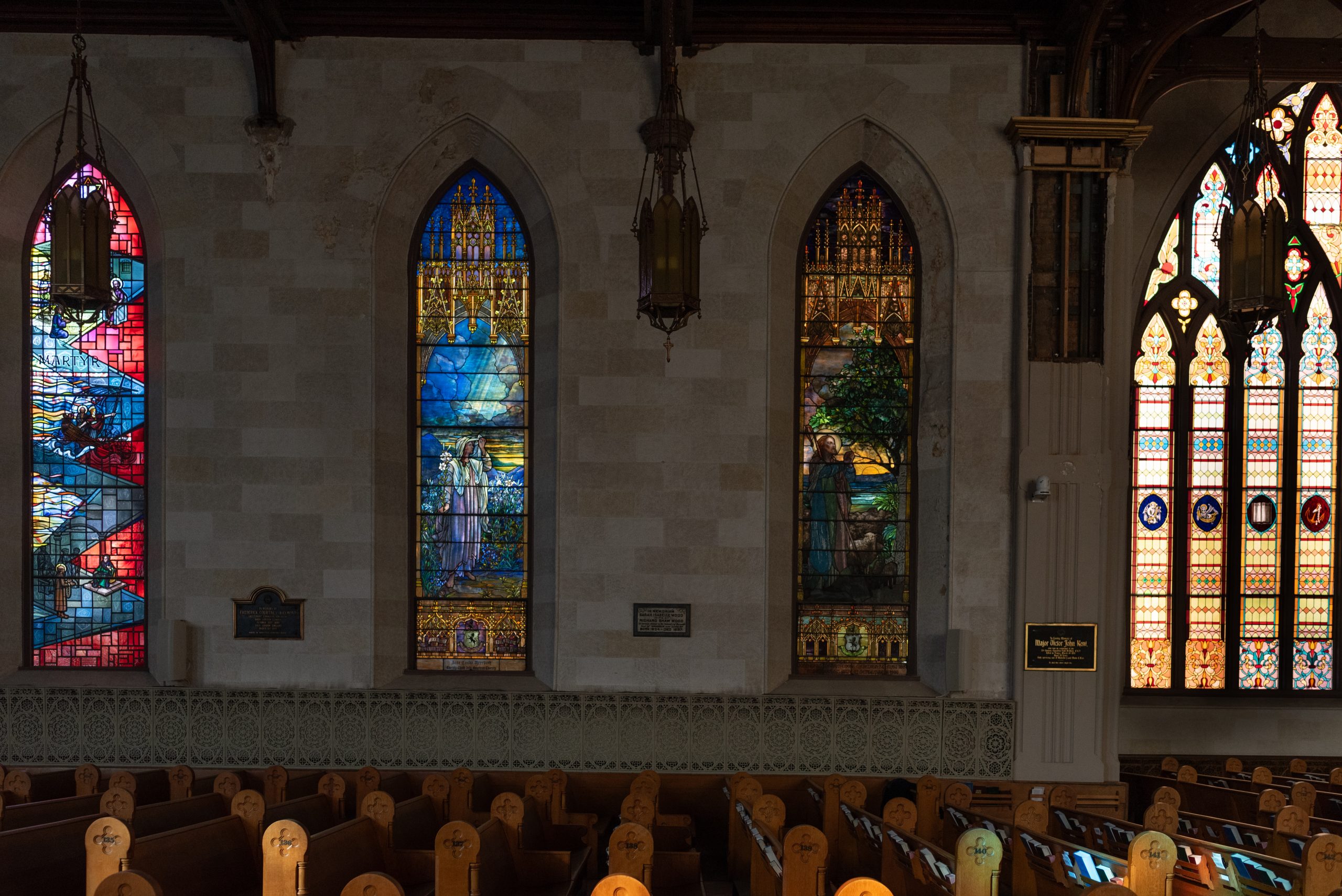 Three stained glass windows. left window is more abstract. centre window shows a divine woman. right window show man and sheep.