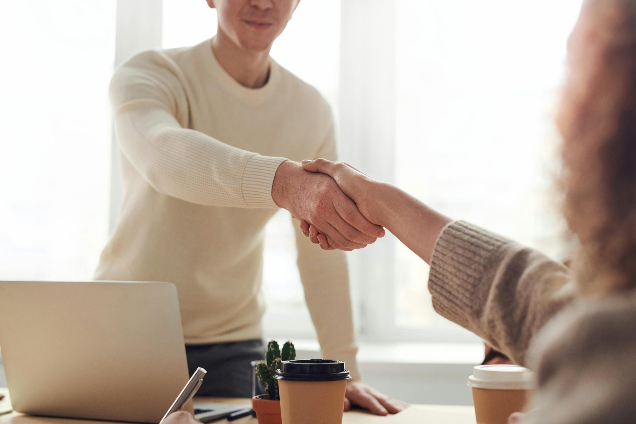 one person standing and the other sitting and shaking hands across the desk