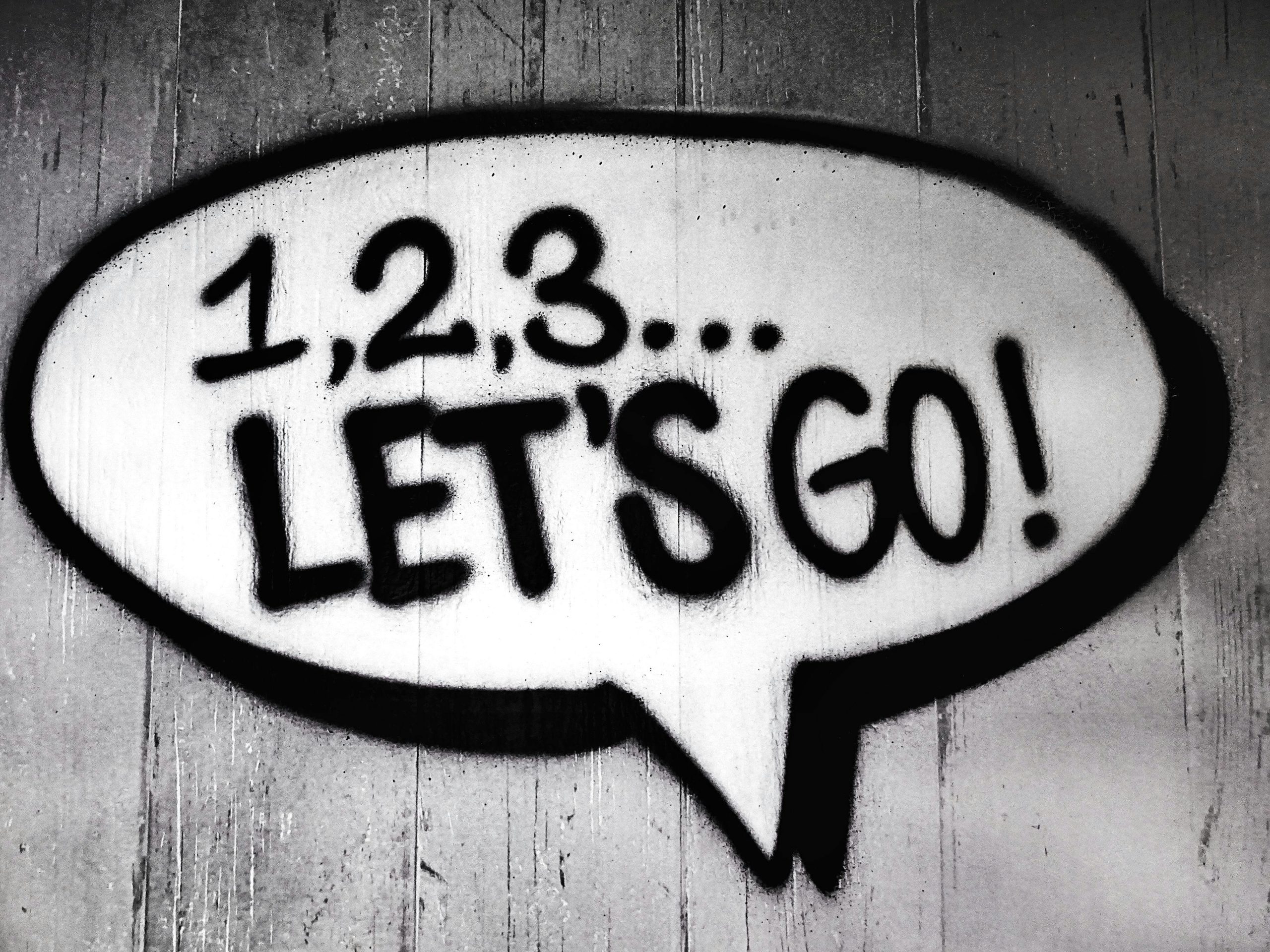 spray painted white speech bubble with black text 1,2,3, Let's go! on concrete wall