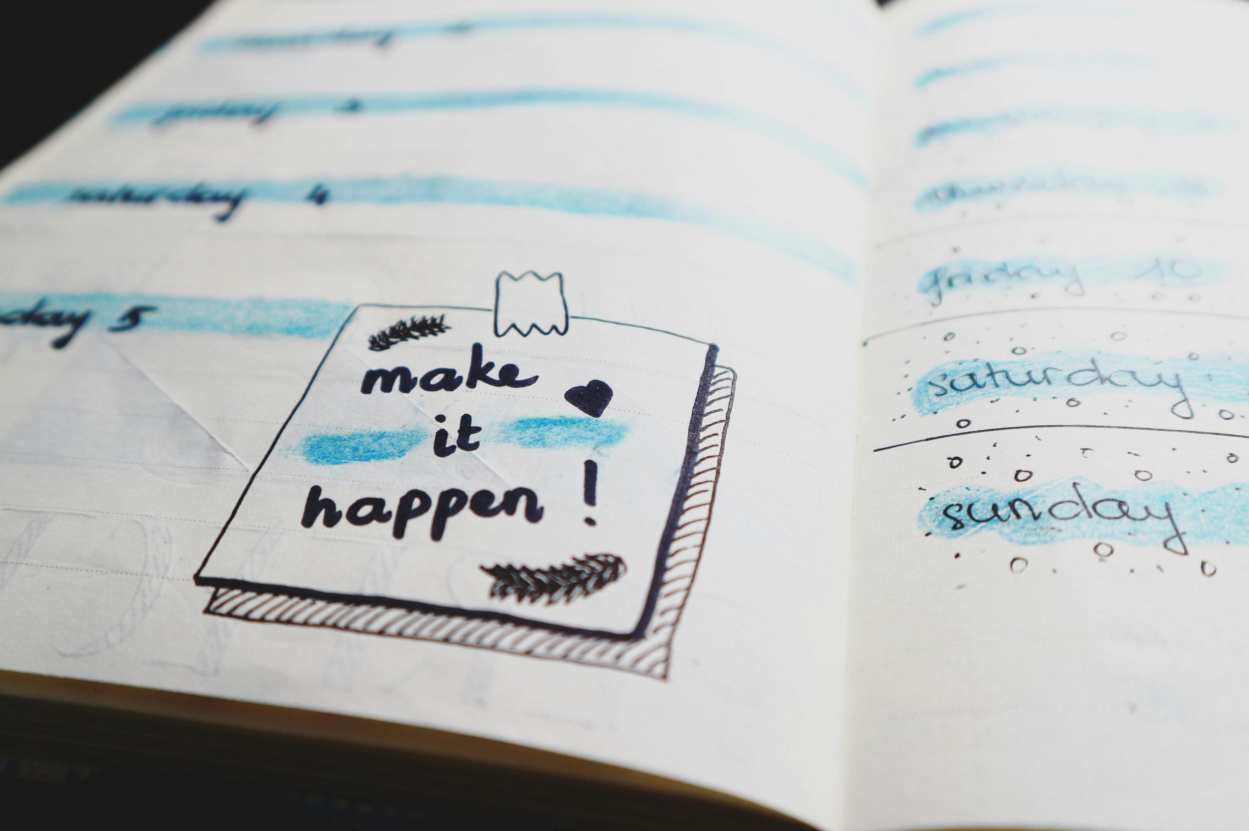 sticky note drawing in notebook that says make it happen in black marker and decorated with blue highlighting