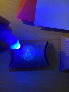 blue light is shining on a package to reveal invisible ink that says A