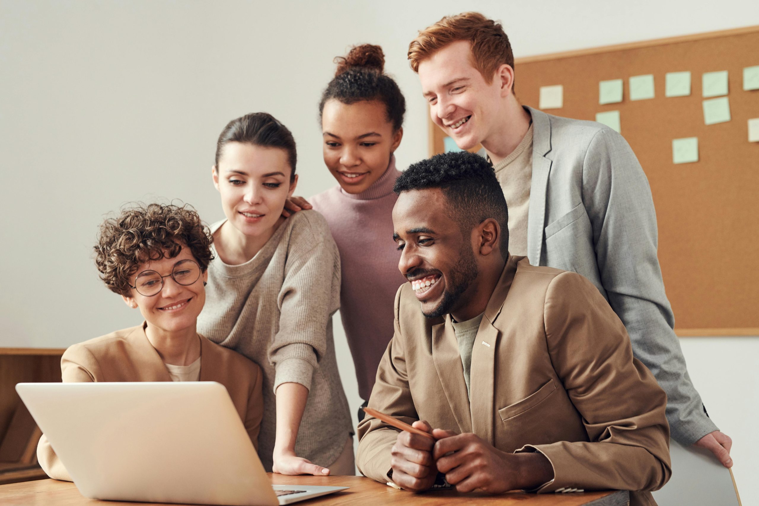 group of 5 adults, 3 standing and two sitting, all facing a laptop on a desk