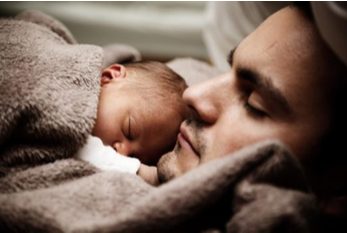 Dad sleeping on their back while holding their sleeping baby on their chest covered by a soft brown blanket