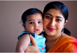 A brown woman holding a baby while looking at the camera.