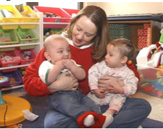 Woman sitting on the floor while smiling and holding two young infants