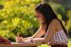 Une jeune étudiante étudie à l’extérieur sur le campus et surligne des notes importantes.
