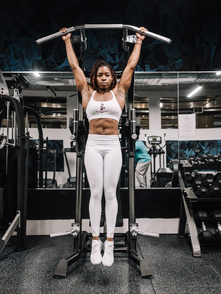 This photo shows a muscular woman-in-white-tank-top-and-white-pants-doing-exercise in a gym.