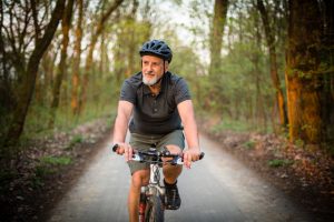 Older man with short and tshirt wearing a bike helmet and cycling on a country road.