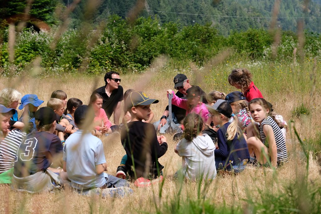 A group of students sitting in a circle outside with 3 adults present
