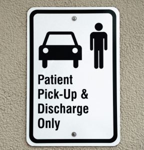 A white rectangular sign with a black outline, black silhouette icons of a car and a person at the top, and the text "Patient Pick-Up and Discharge Only" at the bottom.