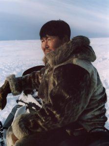 Inuit man in Arctic outdoors kneeling on snow and ice looking into the distance