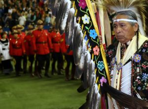 Indigenous leader at a festival, in full regalia, Canadian mounted police in the background