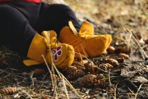 a child's feet, in leather moccasins, sitting against dried leaves and grass