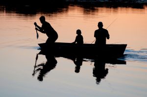 Two adults and a child fishing in a canoe during sunset. Only their silhouette is seen