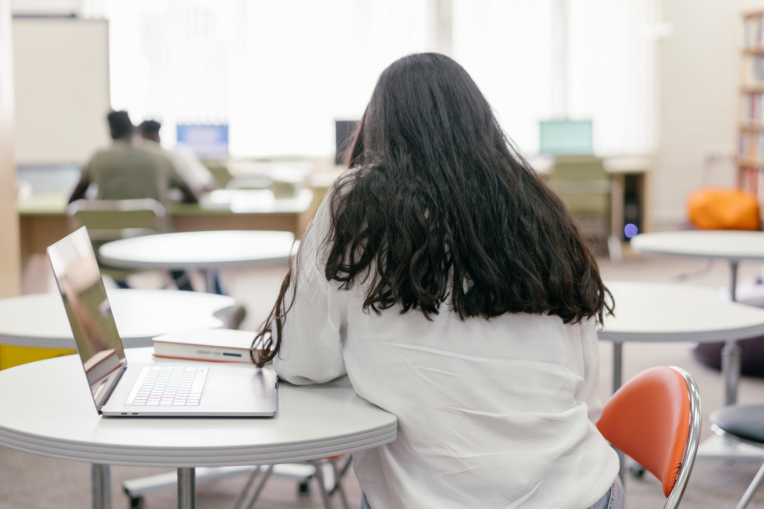 girl sitting at a table with her laptop and book