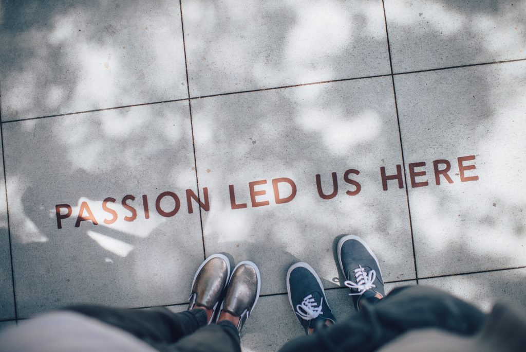 Two sets of feet standing on pavement with the words, "Passion led us here" etched into the cement.