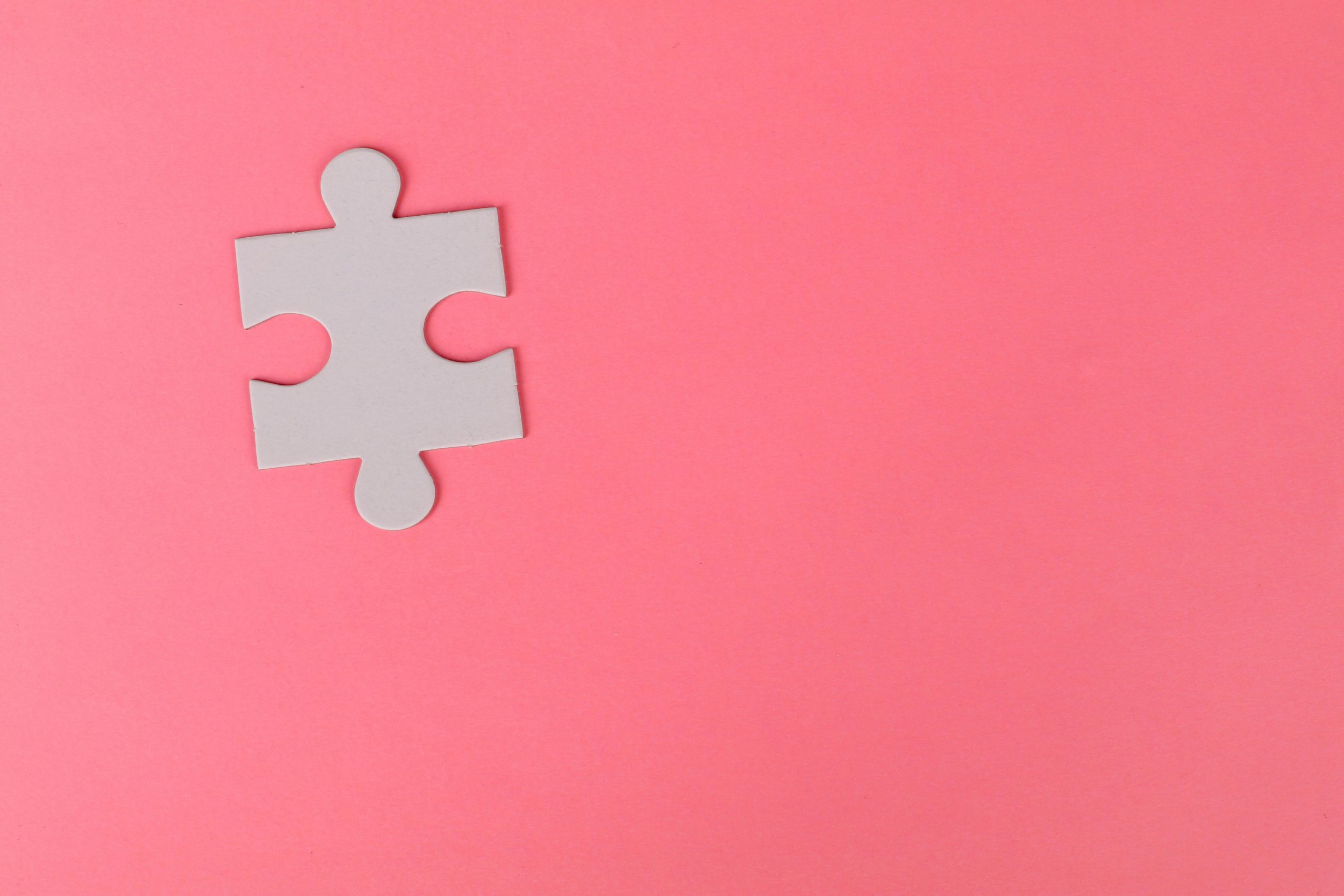 A grey puzzle piece on a bright pink background.