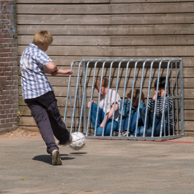boy kicking ball at children in cage