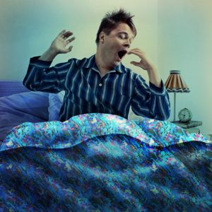 photo of a man in bed yawning and stretching