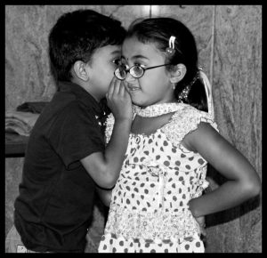 photo of young boy whispering into young girls ear