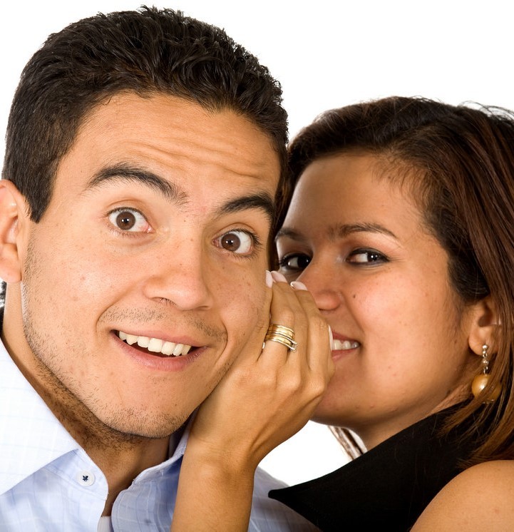 photo of female whispering into mans ear; man looks surprised
