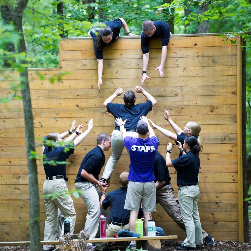 Photo of people working as a team to get over a wood wall