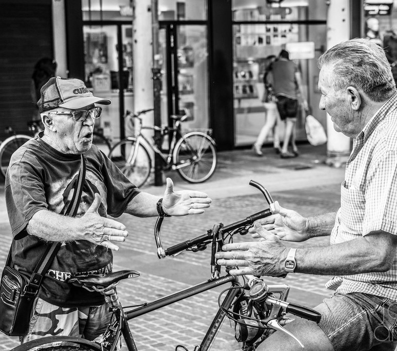 black and white photo of two men talking between a bicycle on the street