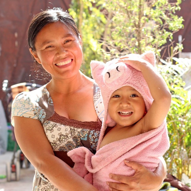 A photo of a mother holding an infant wrapped in a towel. Both are smiling