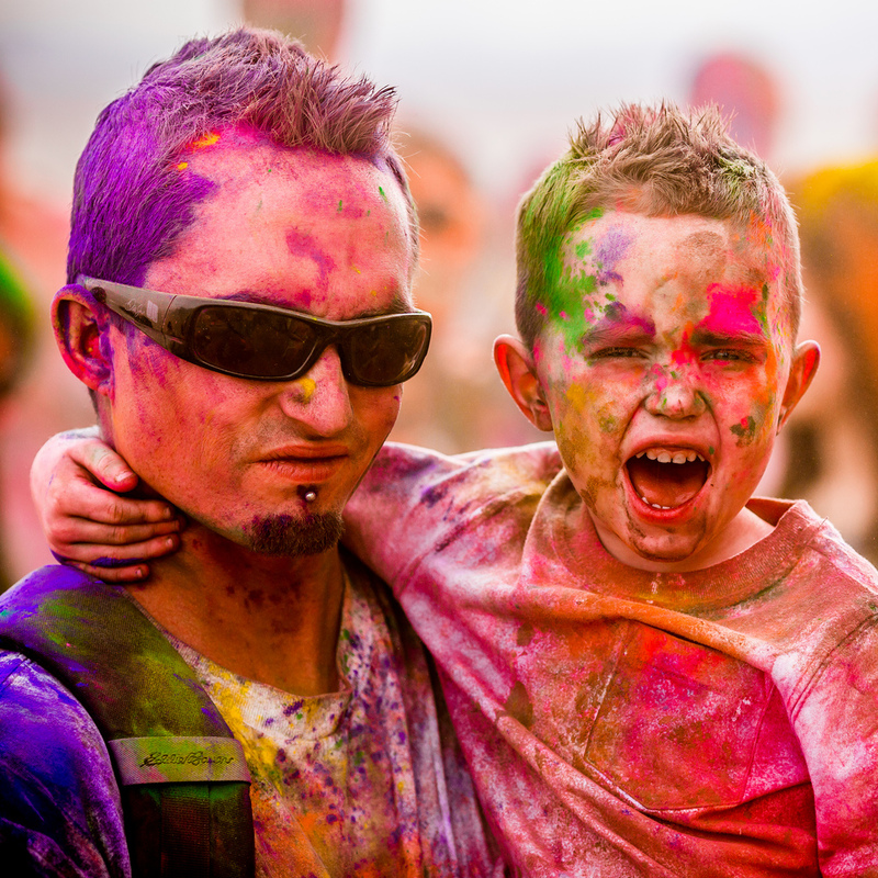 A man holding a child. Child looks like he is yelling, they are covered in colour from what looks like a "colour run"