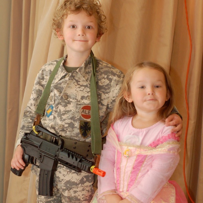 photo of two children, one is dressed in a pink dress the other is dressed in a military uniform holding a plastic gun