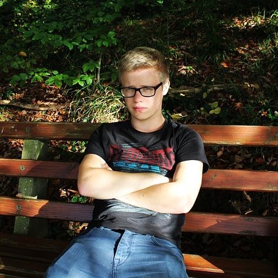 photo of a young male sitting on park bench with arms crossed