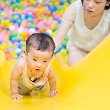 photo of infant climbing up a slide with support for parent