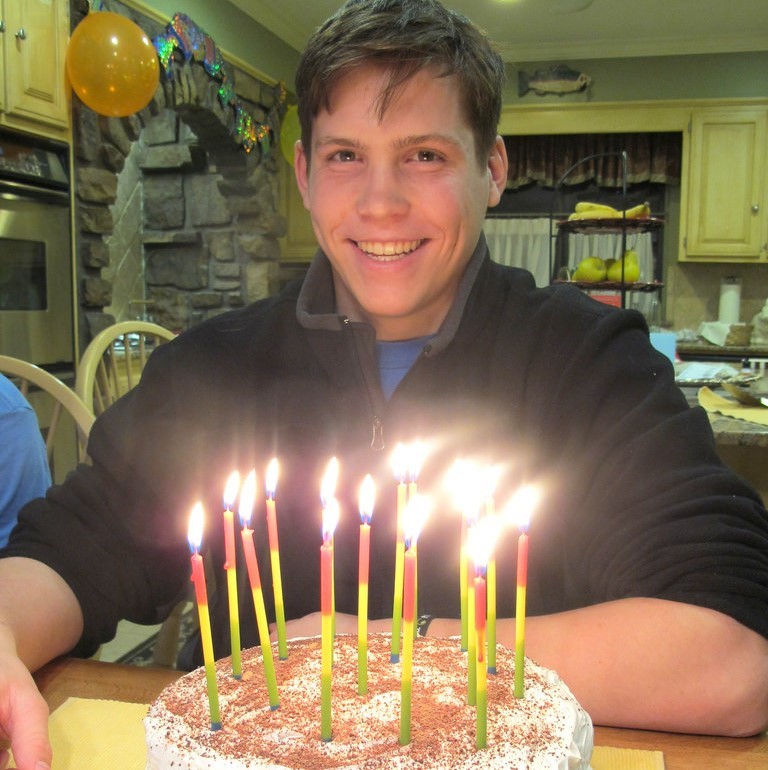 Photo of a man smiling with a birthday cake in front of him