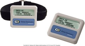 A photo of two personal radiation monitoring badges from Global Dosimetry Solutions, one attached to a strap and the other by itself, displaying identification information for a worker named Joe Smith.